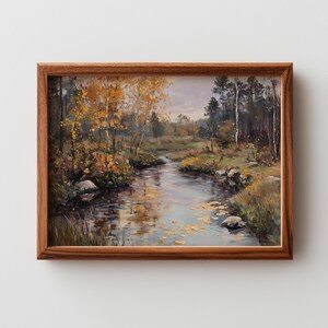 May include: A framed landscape painting depicts a serene river scene. The artwork features a flowing river surrounded by trees with golden autumn foliage. The painting is encased in a brown wooden frame.