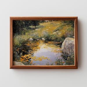 May include: A framed landscape painting depicts a serene pond scene. The artwork features a pond with lily pads, surrounded by lush greenery, rocks, and a grassy bank. The painting is in a wooden frame.
