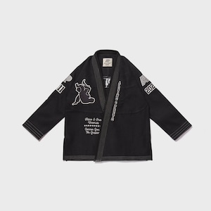 Op de afbeelding: Zwarte vechtsport gi met witte stiksels en patches. De gi heeft een witte afbeelding op de borst en mouwen, samen met de tekst "ALL DAY EVERY DAY" en "202". De gi heeft een traditionele kraag en is gemaakt van een duurzame stof.