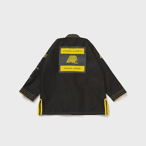 May include: Black martial arts gi with yellow stitching and accents. The back features a rectangular patch with the text "ALBINO & PRETO" above a logo and the words "DOUBLE GOOSE" below. The gi has a traditional collar and sleeve design.