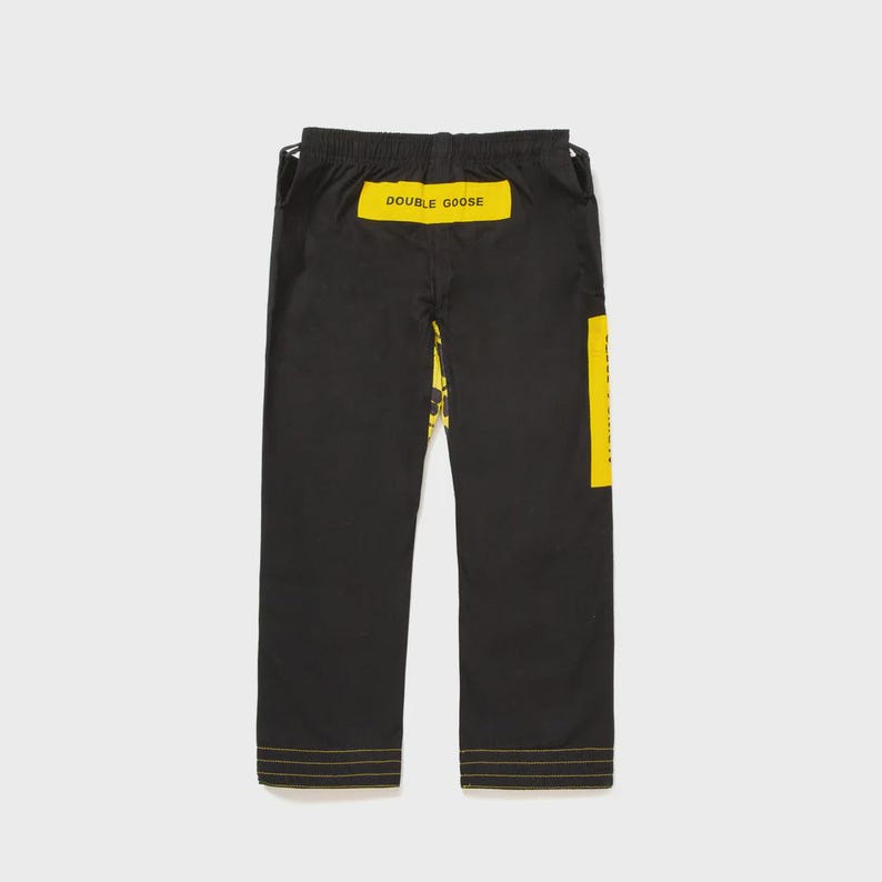May include: Black pants with yellow accents and the text "DOUBLE GOOSE" on the back. The pants have a yellow stripe down the side and yellow stitching along the bottom hem. The pants are made of a durable material.