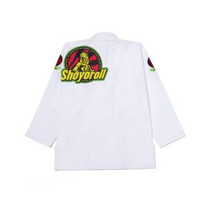 Puede incluir: Kimono de Jiu-Jitsu blanco con el logo de Shoyoroll en la espalda. El logo presenta un león, el texto "Shoyoroll" y la frase "Made Well By Choice Not By Chance - Live Well, Train Well, Thrive Well". El kimono tiene detalles en rojo y verde.