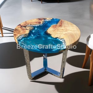 Könnte beinhalten: Runder Couchtisch mit einer Holzplatte und einem blauen Harzfluss-Design. Der Tisch hat ein natürliches Holzmaserungsmuster und steht auf einem silberfarbenen Metallfuß. Der Durchmesser des Tisches beträgt ca. 76 cm.