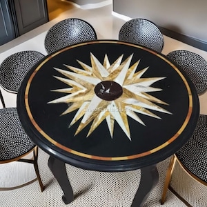 Può includere: Un tavolo rotondo nero con un design a stella in oro e bianco. Il tavolo ha un bordo dorato ed è circondato da sei sedie con sedili a pois bianchi e neri. Le gambe del tavolo sono nere e curve.