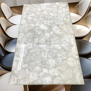 Könnte beinhalten: Ein rechteckiger Esstisch mit einer hellgrauen, mosaikartigen Oberfläche. Der Tisch ist von mehreren Stühlen mit weißen und schwarzen Sitzen und goldfarbenen Rahmen umgeben. Die Tischbeine sind aus Holz.