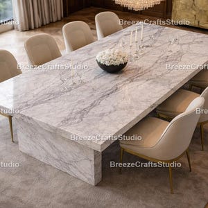 Könnte beinhalten: Ein großer rechteckiger Esstisch aus Marmor mit acht cremefarbenen Stühlen. Der Tisch hat ein grau-weißes Adernmuster. Eine schwarze Schale mit weißen Blumen und Kerzen steht auf dem Tisch. Die Stühle haben goldene Beine.