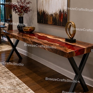 Könnte beinhalten: Ein langer Holztisch mit einem roten Harzfluss-Design. Der Tisch hat eine dunkle Holzoberfläche und schwarze Metallbeine in X-Form. Dekorative Gegenstände, darunter eine goldene Skulptur und eine Schüssel, befinden sich auf dem Tisch.