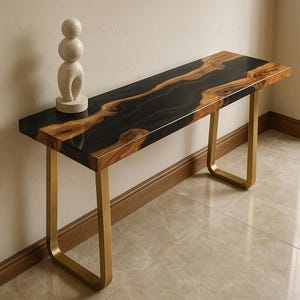 Könnte beinhalten: Eine moderne Konsole mit einer schwarzen Epoxidharzplatte und Akzenten aus natürlicher Holzmaserung. Der Tisch wird von goldfarbenen Metallbeinen getragen und weist eine dekorative Steinskulptur auf. Der Tisch ist etwa 152 cm lang.