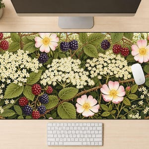 May include: A rectangular desk mat featuring a botanical design with pink flowers, blackberries, and white blossoms on a dark green background. A white computer mouse and keyboard are visible.