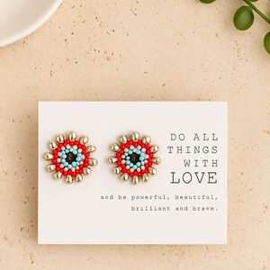 May include: A pair of flower-shaped earrings with red, gold, and turquoise beads. The earrings are displayed on a white card with the text "DO ALL THINGS WITH LOVE" and other inspirational words.
