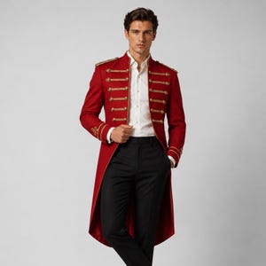 Op de afbeelding: Een rode militair-stijl pandjesjas met goudkleurige gevlochten koorddetails, decoratieve gouden knopen en gestructureerde epauletten op de schouders. Het jasje wordt gedragen over een wit overhemd en een effen zwarte pantalon.