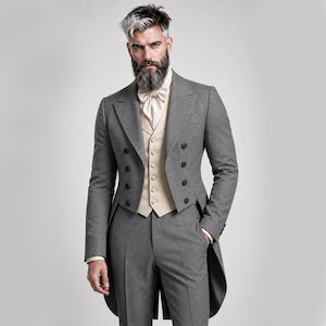 May include: A grey wool morning coat featuring a double-breasted front with black buttons, paired with matching grey trousers and a cream-coloured waistcoat. A cream-coloured cravat is worn at the neck, completing this formal three-piece ensemble.