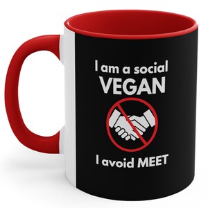 Può includere: Una tazza da caffè rossa e nera con il testo "I am a social VEGAN I avoid MEET" e un cerchio rosso con una linea diagonale che lo attraversa e una stretta di mano all'interno del cerchio.