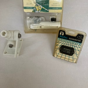 May include: A white plastic flagpole bracket with a nylon adjustable design. The bracket is packaged in a clear plastic bag with the brand name "Toland" and the words "Flagpole Bracket" printed on it. The package also includes a small black plastic cap. A white plastic antenna mount is also shown in the image. A small white and black hour meter is packaged in a clear plastic bag with the brand name "Teleflex" and the words "Hourmeter" printed on it.