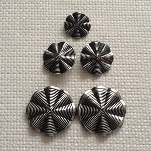 May include: Set of four silver buttons with a concentric circle design. The buttons are different sizes and have a shiny finish.