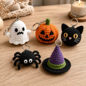 May include: A set of five crochet keychains featuring Halloween themes: a white ghost with black features, an orange pumpkin jack-o'-lantern, a black cat with yellow eyes, a black spider with white eyes, and a purple and green witch hat.