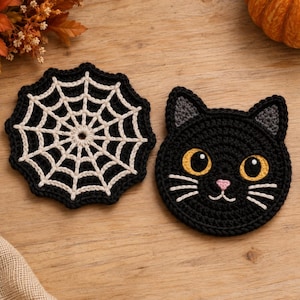May include: Two round crochet coasters. One coaster features a black and cream spiderweb pattern with a scalloped edge. The other coaster is a black cat face with yellow eyes, grey inner ears, a pink nose, and white embroidered whiskers.