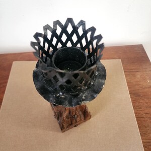 May include: A candle holder featuring a black metal lattice crown top with a ruffled edge, mounted on a textured brown base that resembles a tree trunk. The central cylindrical opening is designed to hold a single candle securely in place.