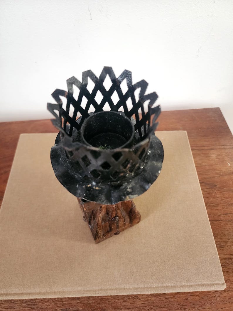 May include: A candle holder featuring a black metal lattice crown top with a ruffled edge, mounted on a textured brown base that resembles a tree trunk. The central cylindrical opening is designed to hold a single candle securely in place.