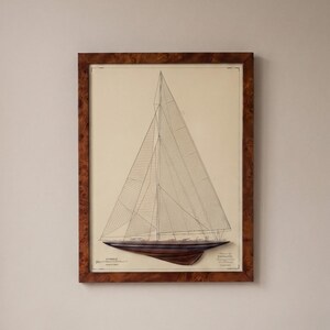 Könnte beinhalten: Gerahmter nautischer Druck mit einer detaillierten Illustration eines Segelboots. Die Kunst ist in schwarzen Linien auf cremefarbenem Hintergrund gehalten, mit einem dunkelbraunen Rumpf. Der Rahmen besteht aus Holz mit einer gemusterten Maserung.
