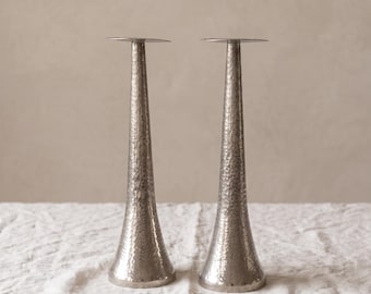 Coppia di portacandele alti in metallo martellato, candelieri affusolati color argento, moderni supporti per candele scultorei, eleganti decorazioni per la tavola.