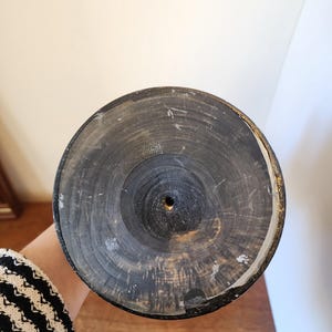 Pode incluir: Uma base circular de madeira com acabamento escuro e carbonizado, exibindo an&eacute;is de crescimento conc&ecirc;ntricos vis&iacute;veis e um pequeno orif&iacute;cio central. A borda do disco apresenta um fino acabamento met&aacute;lico dourado e desgastado ao redor.