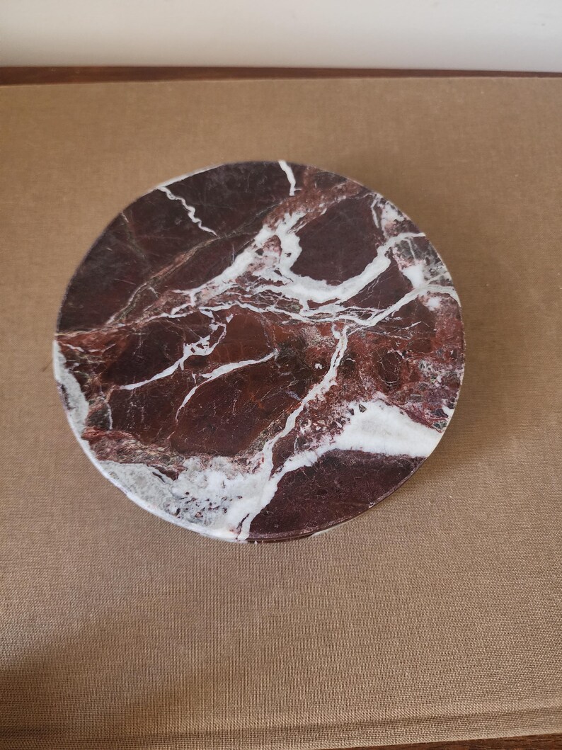 May include: A circular coaster featuring a deep burgundy and dark red marble surface with prominent, irregular white veining throughout. The stone has a polished finish, showcasing the natural color variations and intricate patterns of the marble.