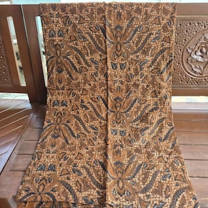 May include: A rectangular piece of fabric featuring a brown and dark gray batik pattern. The design consists of symmetrical floral and leaf motifs arranged in repeating vertical columns, accented by intricate dotted textures throughout the surface.