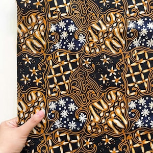 Könnte beinhalten: Ein Stoffstück mit einem sich wiederholenden Batikmuster in Schwarz, Dunkelblau und Goldgelb. Das Design besteht aus stilisierten Blumenmotiven und komplexen, geschwungenen Linien, die ein dichtes, miteinander verbundenes geometrisches Layout bilden.