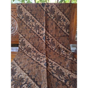 Könnte beinhalten: Ein brauner Stoff mit einem sich wiederholenden diagonalen Muster aus dunkelbraunen Blumenmotiven und komplizierten Blattdesigns. Das Textil weist eine strukturierte Optik mit einem dichten, detaillierten Druck auf.