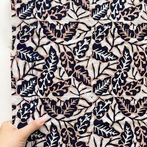Peut inclure: Un morceau de tissu présentant un motif botanique répétitif avec des feuilles bleu marine foncé, des feuilles rose clair et des contours de feuilles blancs. Le motif est dense et couvre toute la surface du textile avec un style graphique plat.