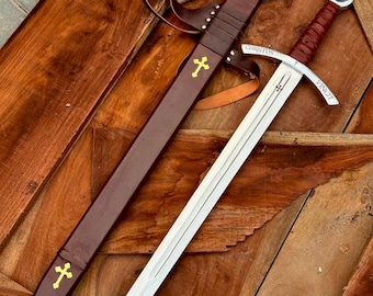 May include: A medieval-style sword with a silver blade and a brown leather-wrapped handle. The sword is accompanied by a brown leather sheath with a gold cross emblem. The word "CHRISTUS" is etched on the blade.