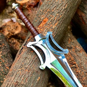 Può includere: Una spada a doppio taglio con una lama in metallo color argento lucido e una guardia complessa e curva. L'impugnatura è rivestita in pelle marrone scuro e presenta un pomolo metallico all'estremità, con una finitura nitida e riflettente.