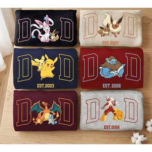 Może przedstawiać: Sześć bluz z napisem "DAD" w czcionce uniwersyteckiej. Każda bluza przedstawia inną postać lub postacie z Pokemonów. Bluzy są w różnych kolorach, w tym czarnym, granatowym, czerwonym i szarym.