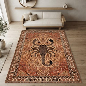 Può includere: Un tappeto rettangolare caratterizzato da una grande grafica di scorpione marrone scuro centrata su uno sfondo caldo color arancione e marrone chiaro. Il tappeto presenta intricati motivi geometrici e bordi in tonalità di marrone, beige e arancione.