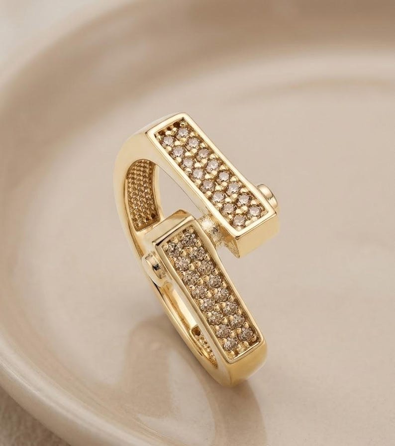 May include: A gold-colored, hinged clasp with two rectangular sections encrusted with small, sparkling stones. The clasp is set against a soft, neutral background, highlighting its intricate design and polished finish. The jewelry piece is likely used for necklaces or bracelets.