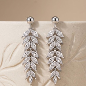 May include: A pair of silver-toned drop earrings. Each earring features a small, round stud at the top, connected to a series of marquise-cut, clear gemstones arranged in a leaf-like design. The earrings are designed to dangle.