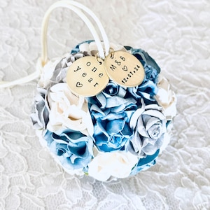 ball shaped ornament made from blue, white and silver paper flowers.  There are personalized charms attached to an ivory satin hanger.  The charms read "one year" for a 1st anniversary gift, and a couples' initials and wedding date.