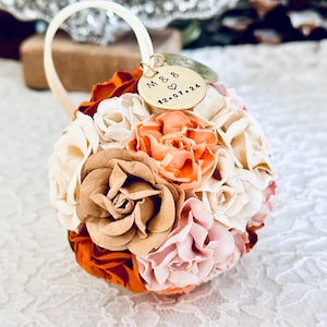 a 1st anniversary ornament made from paper flowers in custom shades of ivory, blush, peach, clay, and terra cotta.  The Christmas ornament has 2 custom charms, engraved with "one year" anniversary and a couples' initials and wedding date.