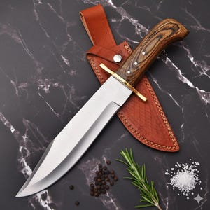 May include: A large hunting knife with a polished steel blade and a wooden handle. The knife rests in a brown leather sheath with a brass guard. The handle has three white rivets. The knife is on a black marble surface.