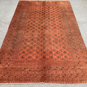 May include: An orange and brown rectangular rug with an intricate geometric pattern. The rug features a central medallion design surrounded by a detailed border. The rug is made of woven material and has a fringed edge.