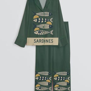 May include: Green pajama set with a collared top and matching pants. The set features a repeating pattern of stylized fish with lemon slices. The word "SARDINES" is printed on the top and bottom of the set.