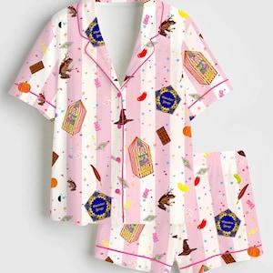 May include: A short-sleeved button-down pyjama shirt and matching shorts set featuring a light pink and white vertical striped pattern. The fabric is decorated with colourful illustrations of chocolate frogs, candy boxes, pumpkins, and hats.