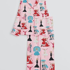 May include: Pink pajama set with a repeating pattern of illustrated figures in various outfits. The long-sleeved top and pants are trimmed with red piping. The pajama set features a button-down top and elastic waist pants.