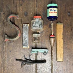 May include: A collection of vintage items including a large metal letter S, a harmonica, two glass jars filled with nails and screws, a Vicks VapoRub jar, a fishing bobber on a stick, a small light blue toy trailer, and a wooden folding ruler.