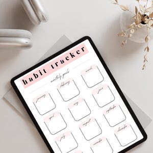 Könnte beinhalten: Ein digitaler Gewohnheitstracker mit schwarzem Rand und weißem Hintergrund. Der Titel "habit tracker" ist rosa, darunter die Worte "monatliche Ziele". Die Monate des Jahres sind in Kästchen aufgelistet. Ein weißer Kopfhörer und eine Vase mit getrockneten Blumen sind im Hintergrund.