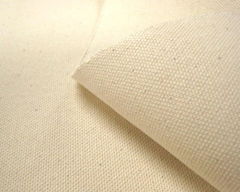May include: A piece of off-white, unbleached canvas fabric with a visible, tight woven texture. The material is folded over to reveal the thickness and the consistent, grainy surface pattern of the heavy-duty textile weave throughout the fabric.