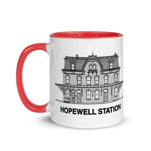 May include: White ceramic mug with a red rim. The mug features a black and white illustration of the Hopewell Station building with the text "HOPEWELL STATION" printed below the illustration.
