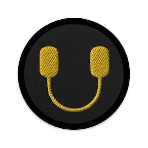 Puede incluir: Un parche bordado negro y amarillo con un diseño de auriculares. Los auriculares son amarillos y el fondo es negro.