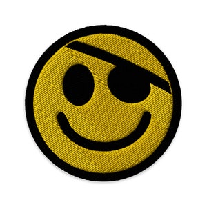 May include: Yellow smiley face with a black eyepatch, embroidered on a black fabric background.